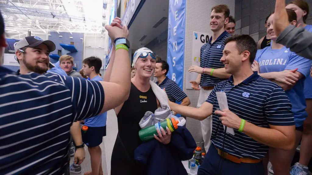 Swim Camps instruction staff high five a swimmer in a swim cap and suit by the pool.