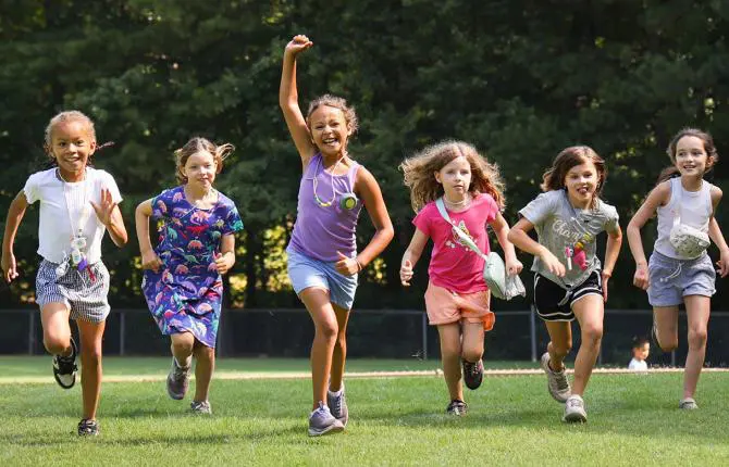 Young campers part of YMCA Day Camp Programming are smiling as they run across the green field playing a camp game.