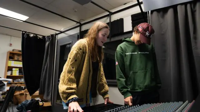 Two students are looking down at a music soundboard inside of a music studio on NC State's campus.
