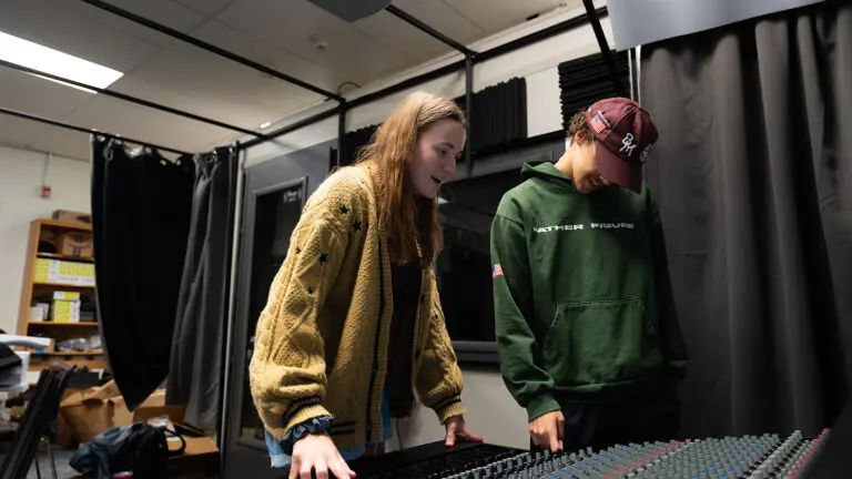 Two students are looking down at a music soundboard inside of a music studio on NC State's campus.