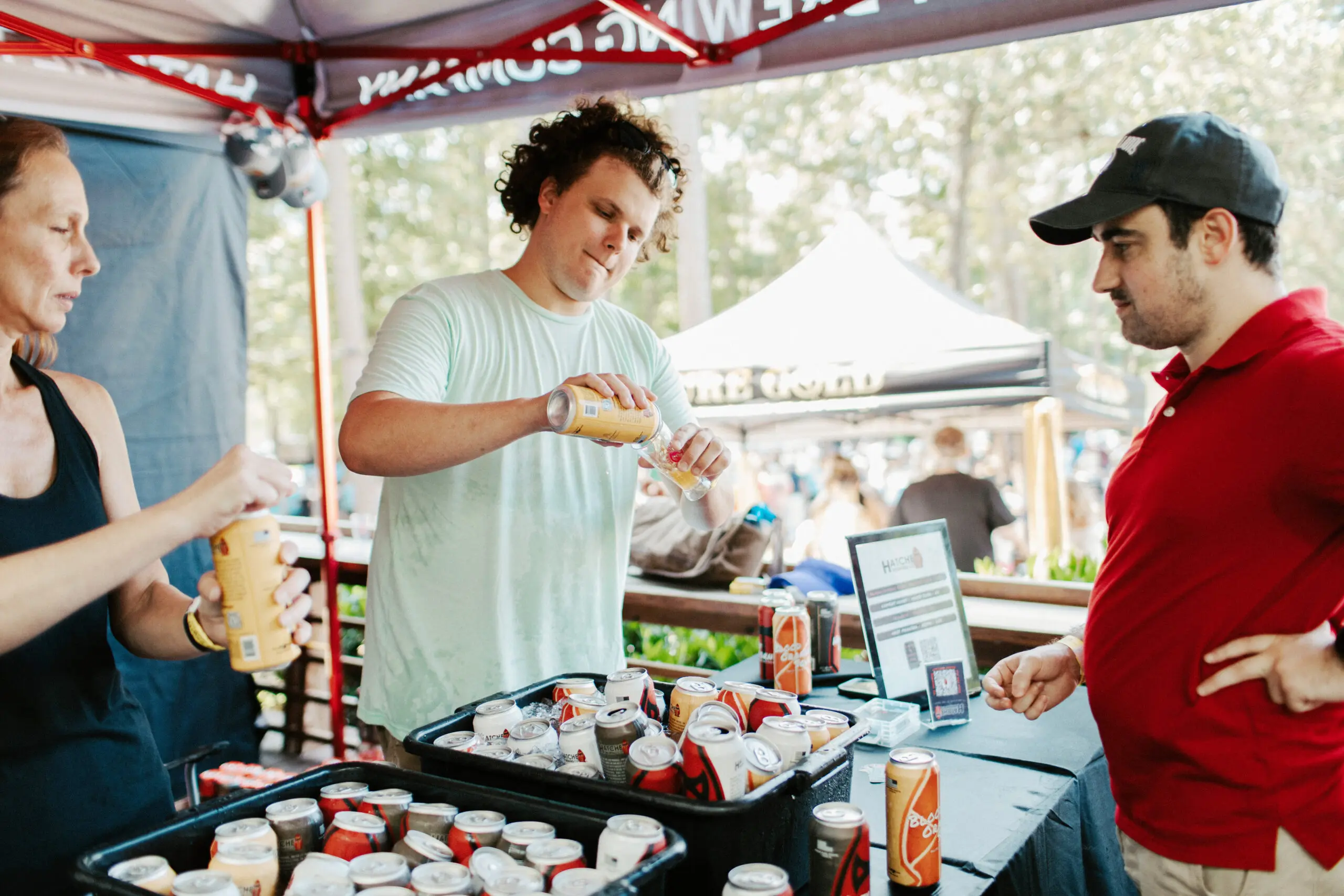 Two people behind a table under a tent pour beer into a glass for a customer.