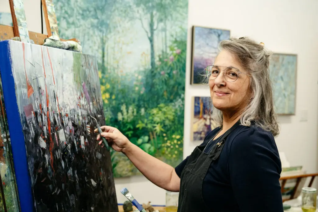 Leslie Pruneau poses for the camera with a big smile as she works on a painting